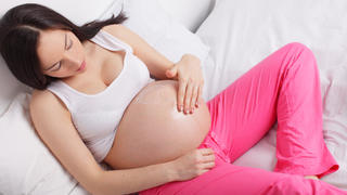 Pregnant woman putting a cream on a stomach at home