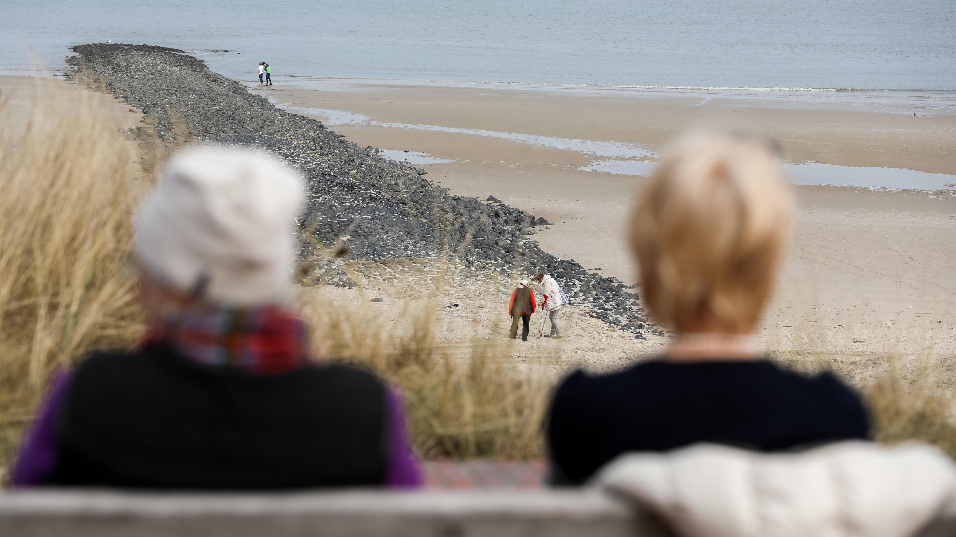 08.04.2018, Niedersachsen, Wangerooge: Zwei Frauen sitzen auf einer Bank und schauen zum Strand. Foto: Mohssen Assanimoghaddam/dpa
