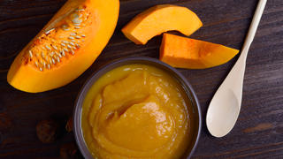 Bowl with pumpkin puree, surrounded by pieces of pumpkin, top view