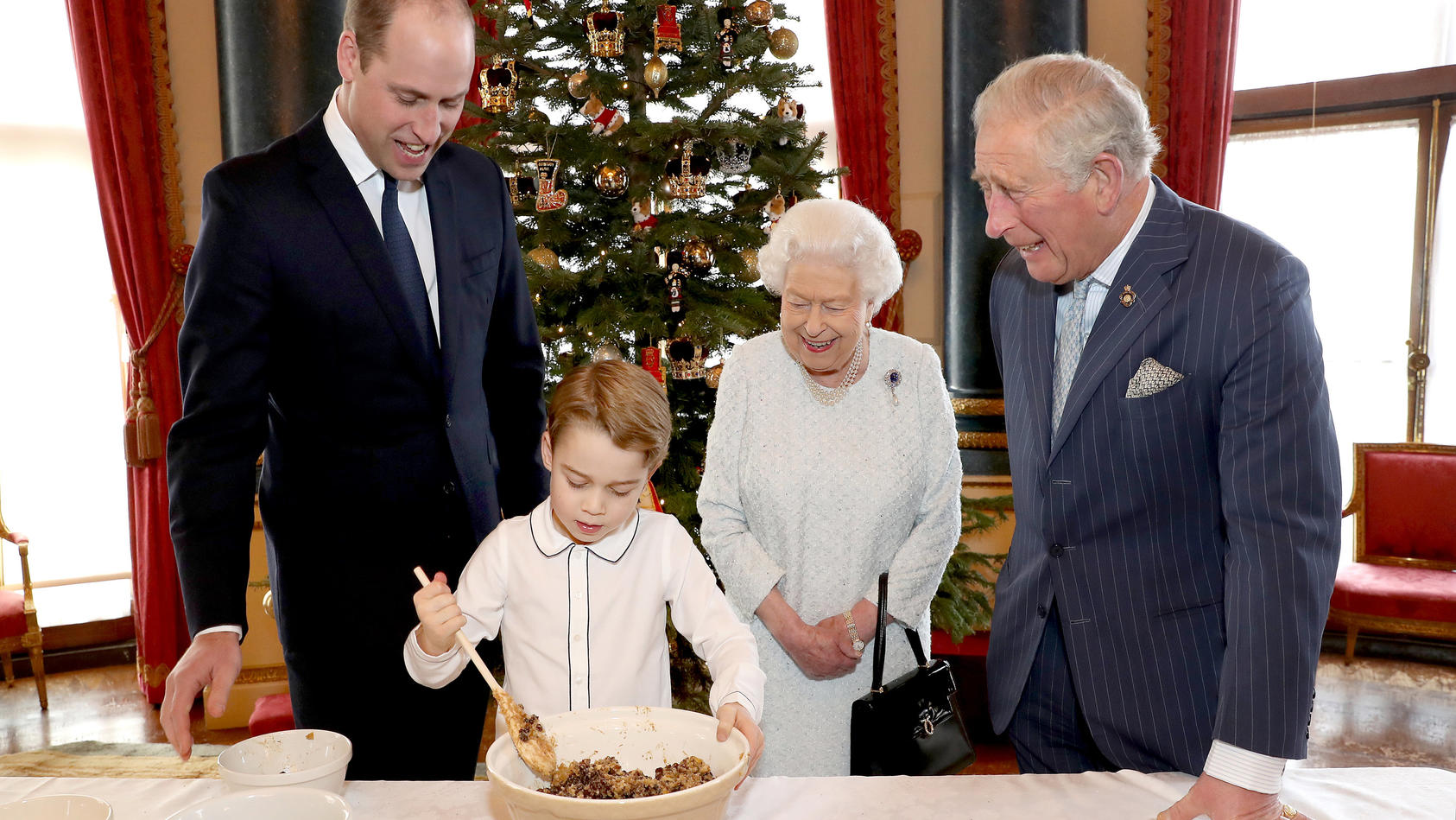 dpatopbilder - HANDOUT - 18.12.2019, Großbritannien, London: Die volle Aufmerksamkeit seines Vaters Prinz William (l), seiner Urgroßmutter Königin Elizabeth II. und seines Großvaters Prinz Charles (r) hat der kleine Prinz George bei der Zubereitung d