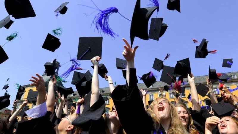 Absolventen einer Universität werfen ihre "Doktorhüte" in die Luft. 