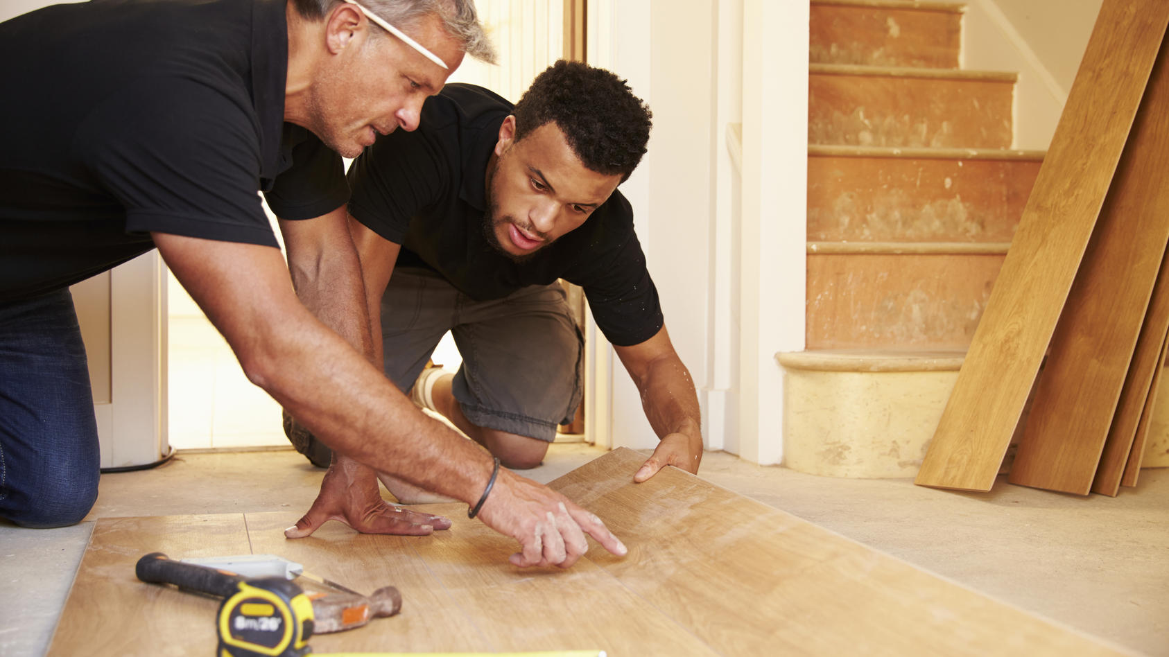 Two men laying wood panel flooring in a house