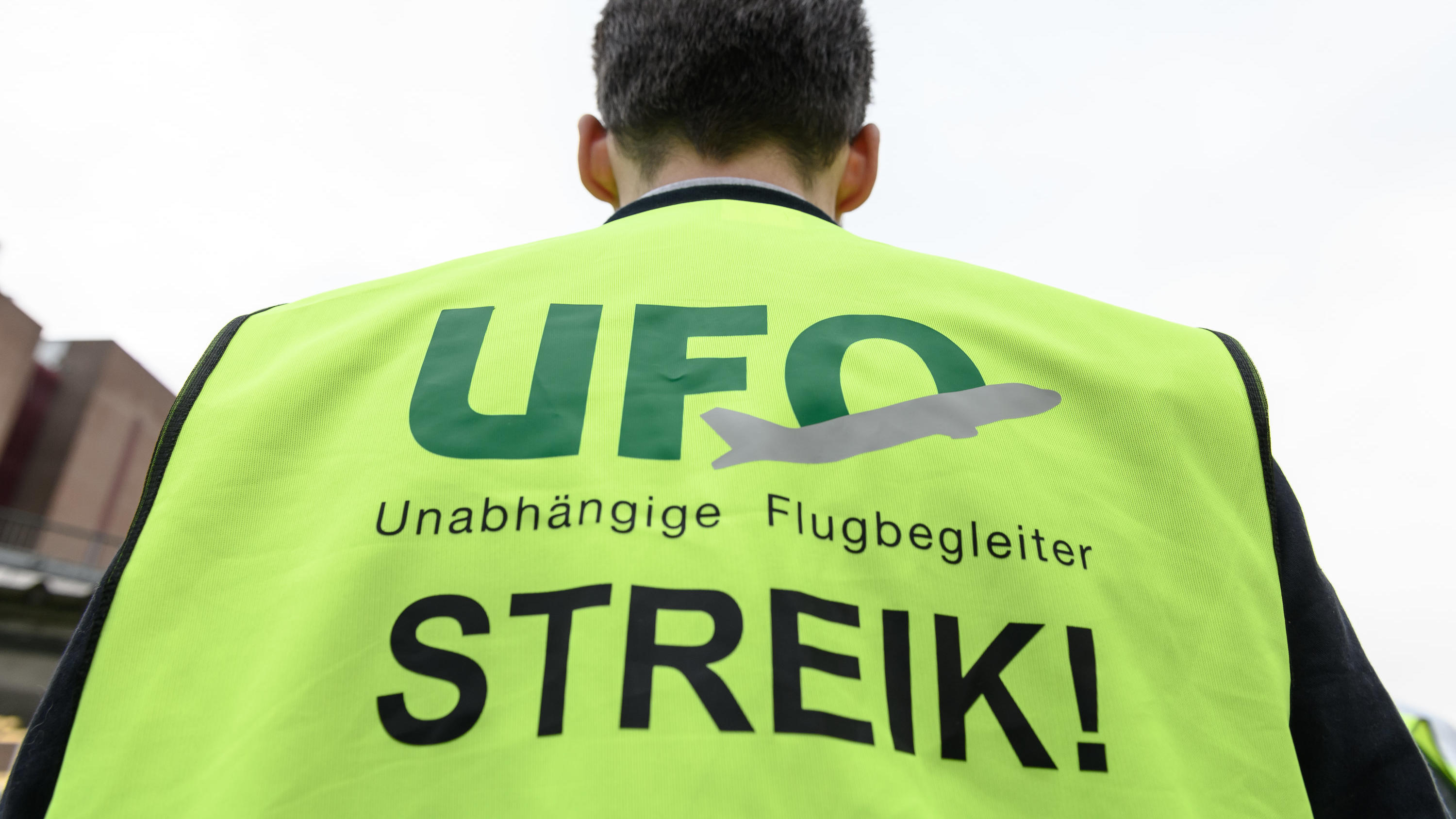 ARCHIV - 20.10.2019, Hessen, Frankfurt/Main: Ein Mann steht mit einer Warnweste mit der Aufschrift «Streik» an Tor 20 des Frankfurter Flughafens. Die Kabinengewerkschaft Ufo hat einen weiteren Streik der Flugbegleiter im Lufthansa-Konzern angekündigt