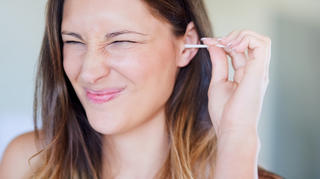 Shot of young woman pulling a funny face while cleaning her ear with an earbud at home