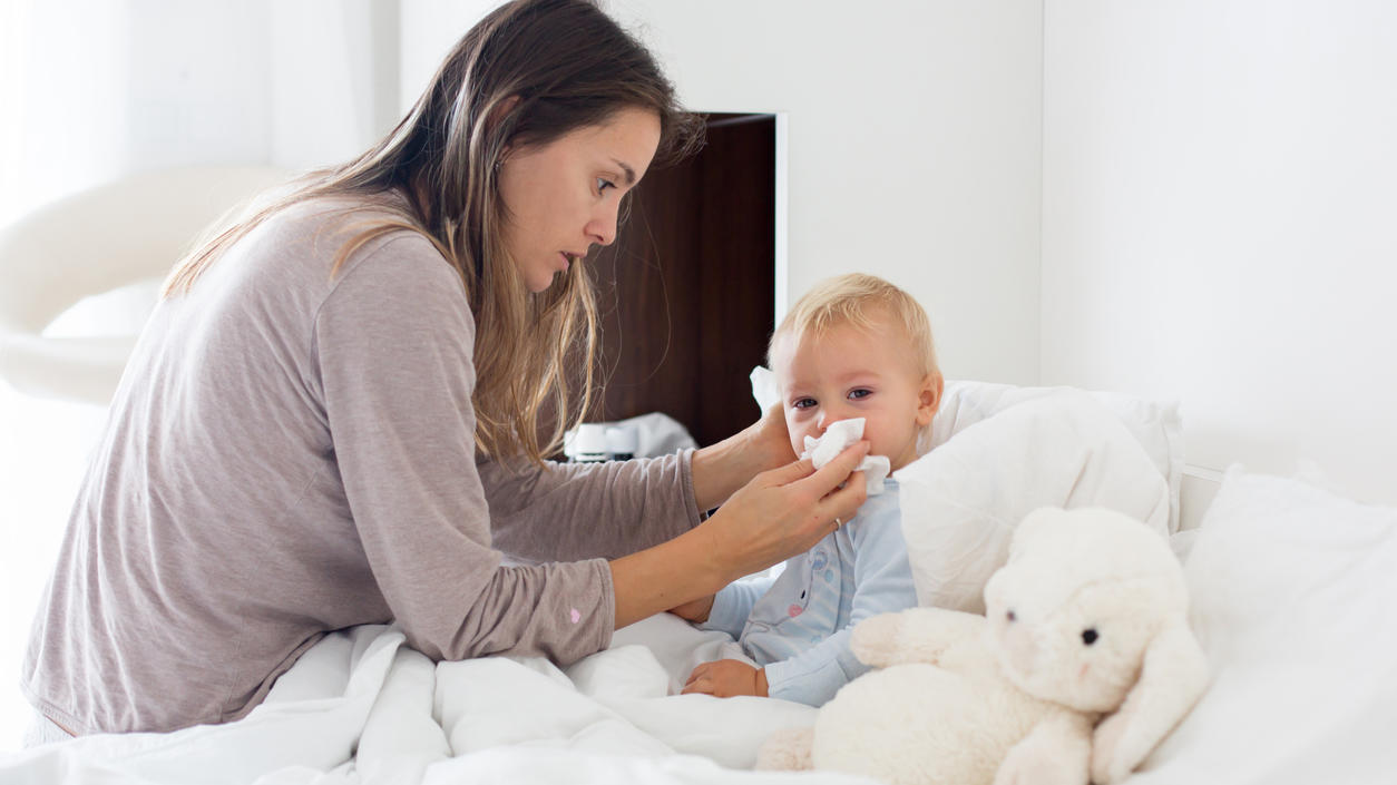 Mother and baby in pajamas, early in the morning, mom taking care of her sick toddler boy. Baby in bed with fever and running nose (Mother and baby in pajamas, early in the morning, mom taking care of her sick toddler boy. Baby in bed with fever and r