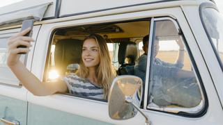 Smiling woman taking a selfie in a camper van with man driving model released Symbolfoto PUBLICATIONxINxGERxSUIxAUTxHUNxONLY GUSF01426  