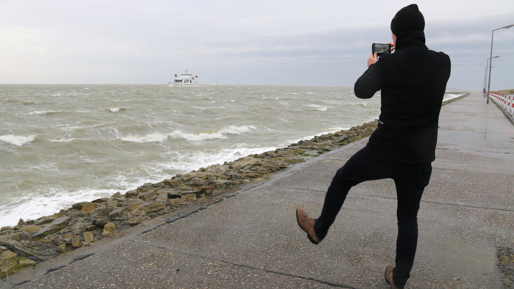 09.02.2020, Niedersachsen, Norderney: Ein Mann macht auf der Strandpromenade auf der Nordseeinsel Norderney ein Foto von der vorbeifahrenden Autofähre. Die ersten Ausläufer des Sturmtiefs "Sabine" haben die Nordsee erreicht. Foto: Volker Bartels/dpa