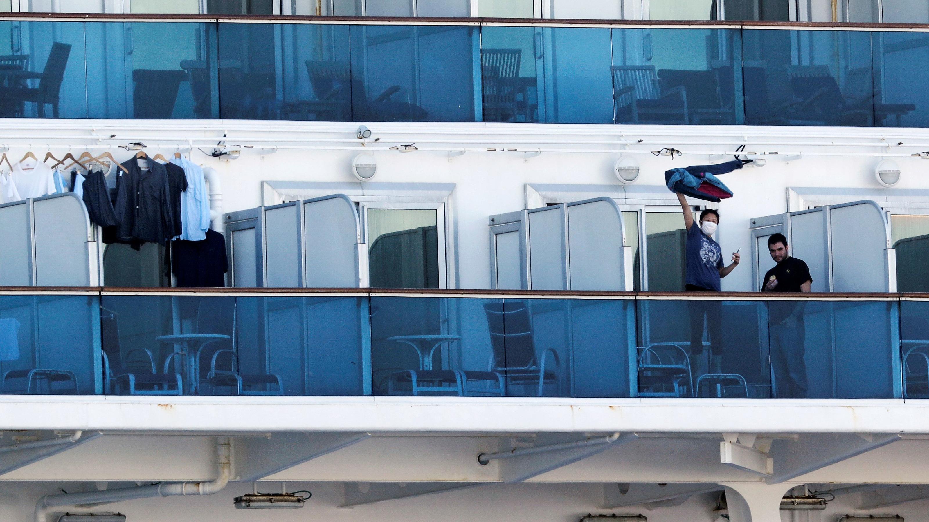 A passenger waves a jacket towards a woman (not pictured) on land as they communicate via phone at the balcony of a cabin on the cruise ship Diamond Princess, as the vessel's passengers continue to be tested for coronavirus, at Daikoku Pier Cruise Te