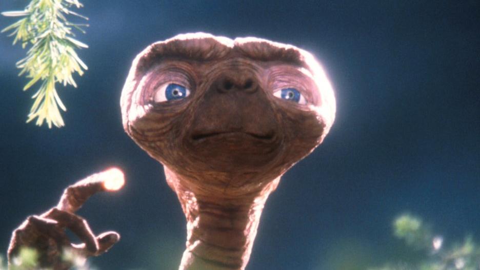 Der Außerirdische "E.T." steht in einer Szene des gleichnamigen Fantasy-Films von Steven Spielberg mit leuchtendem Finger hinter einem Gebüsch. 