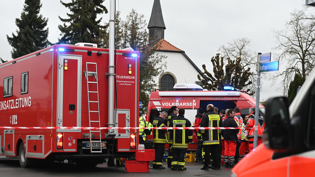 24.02.2020, Hessen, Volkmarsen: Feuerwehrleute und Notfallsanitäter stehen hinter einem Absperrband an der Stelle, an der ein Auto in einen Rosenmontagsumzug gefahren ist. Dabei gab es mehrere Verletzte. Die Polizei hat nach eigenen Angaben noch kei