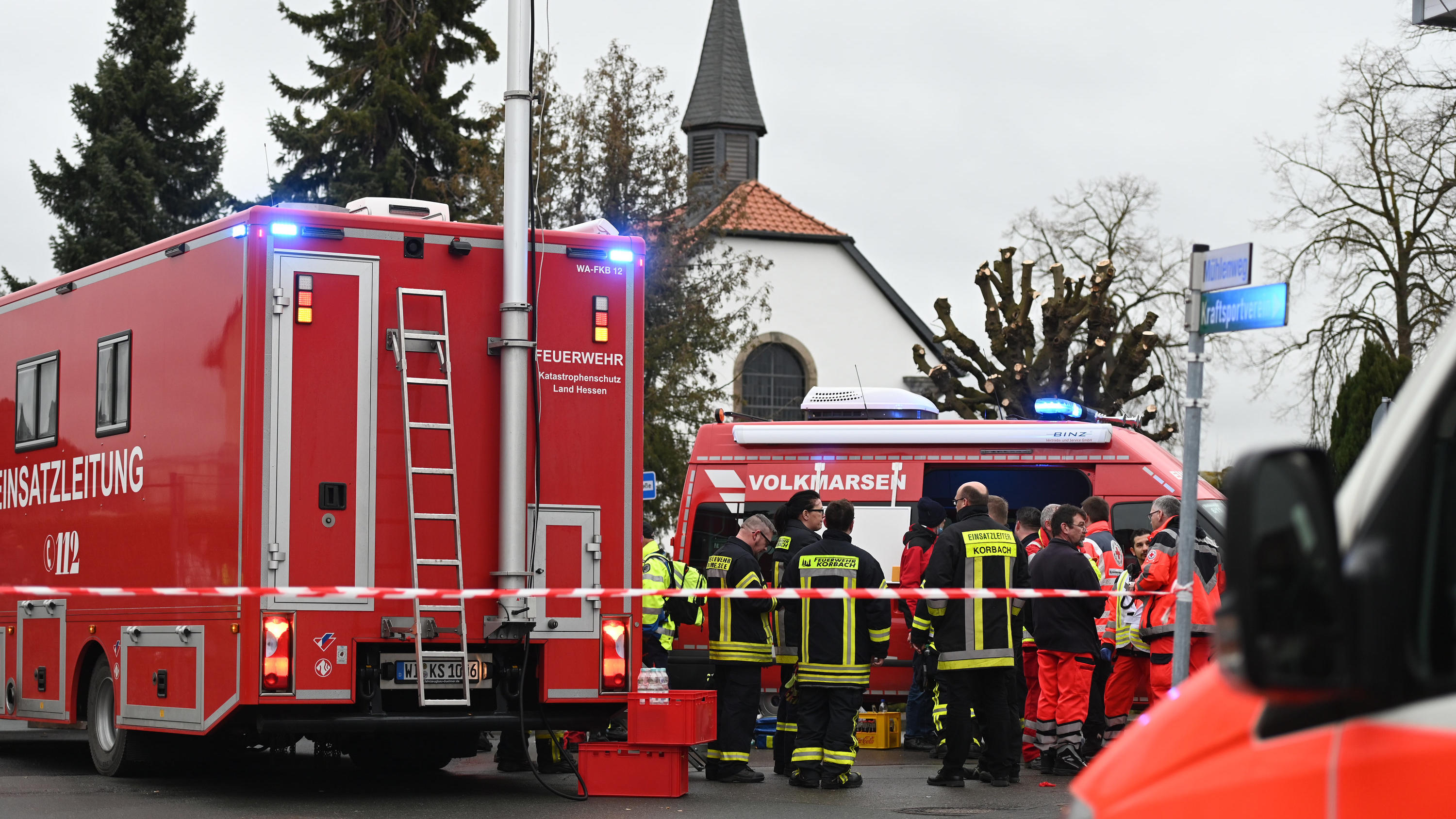 24.02.2020, Hessen, Volkmarsen: Feuerwehrleute und Notfallsanitäter stehen  hinter einem Absperrband an der Stelle, an der ein Auto in einen Rosenmontagsumzug gefahren ist. Dabei gab es mehrere Verletzte. Die Polizei hat nach eigenen Angaben noch kei