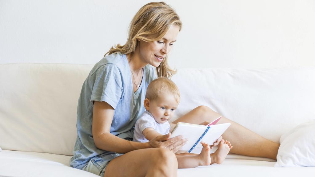 Mother and baby girl sitting on couch looking at picture book model released Symbolfoto property released PUBLICATIONxINxGERxSUIxAUTxHUNxONLY TCF05872
