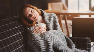 Frau liegt mit Decke auf dem Sofa