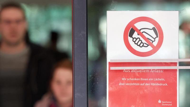 "Aus Aktuellem Anlass: Wir schenken Ihnen einen Lächeln, aber verzichten auf den Händedruck" steht auf einer Glastür einer Sparkasse. Foto: Bernd Thissen/dpa