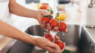 Frau wäscht Tomaten in der Spüle.
