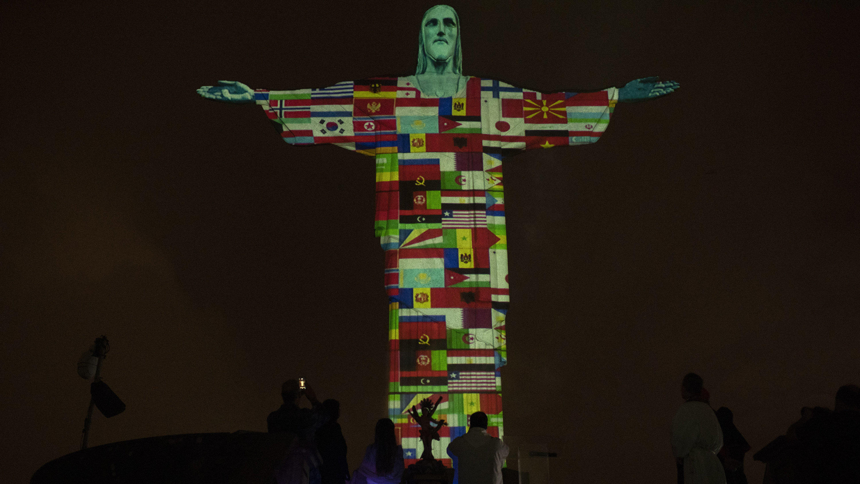 18.03.2020, Brasilien, Rio De Janeiro: Die Christusstatue (Cristo Redentor) ist mit Flaggen der Länder beleuchtet, die derzeit vom neuen Coronavirus befallen sind. Foto: Silvia Izquierdo/AP/dpa +++ dpa-Bildfunk +++