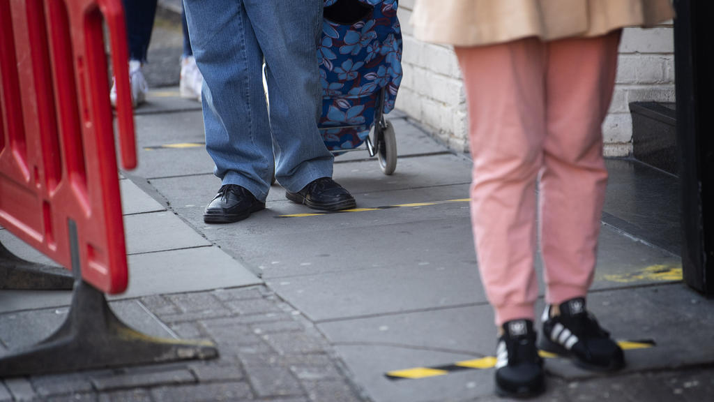 26.03.2020, Großbritannien, London: Kunden stehen vor einem Supermarkt in Westminster Schlange, vor dem Klebeband auf dem Boden angebracht ist, um die Einhaltung eines Mindestabstandes zwischen den Kunden zu gewährleisten. Der britische Premier Johns