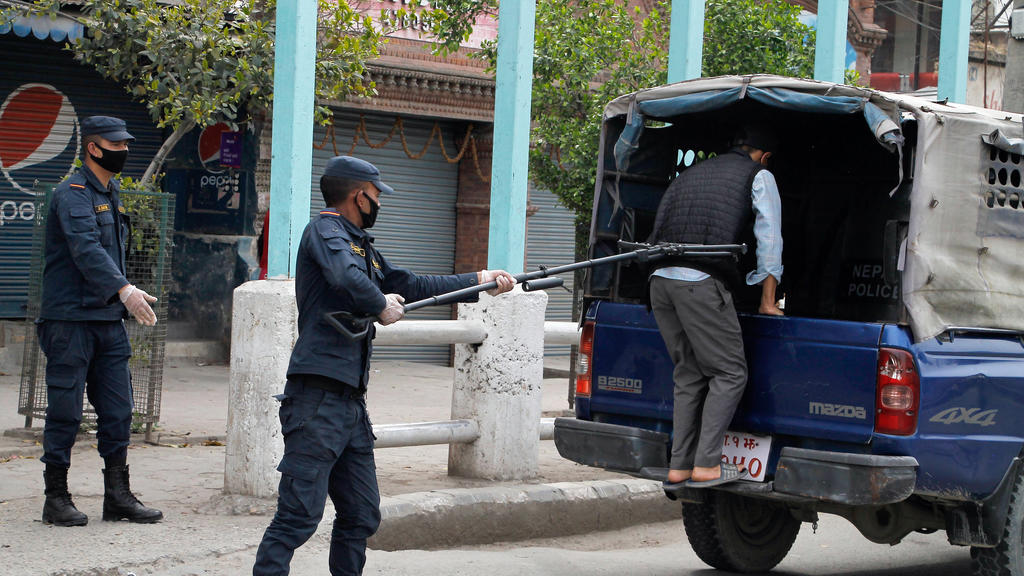 HANDOUT - 27.03.2020, Nepal, Kathmandu: Ein Polizist benutzt einen Abstandshalter, um einen Mann in ein Polizeifahrzeug zu schieben. Foto: Manoj Bhusan Khadka/Polizei Nepal/dpa - ACHTUNG: Nur zur redaktionellen Verwendung im Zusammenhang mit der aktu
