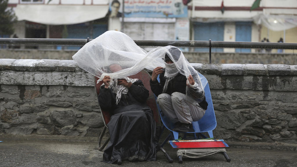06.04.2020, Afghanistan, Kabul: Männer tragen Schals vor dem Gesicht und bedecken sich im Regen mit einer Plastikfolie. Foto: Rahmat Gul/AP/dpa +++ dpa-Bildfunk +++
