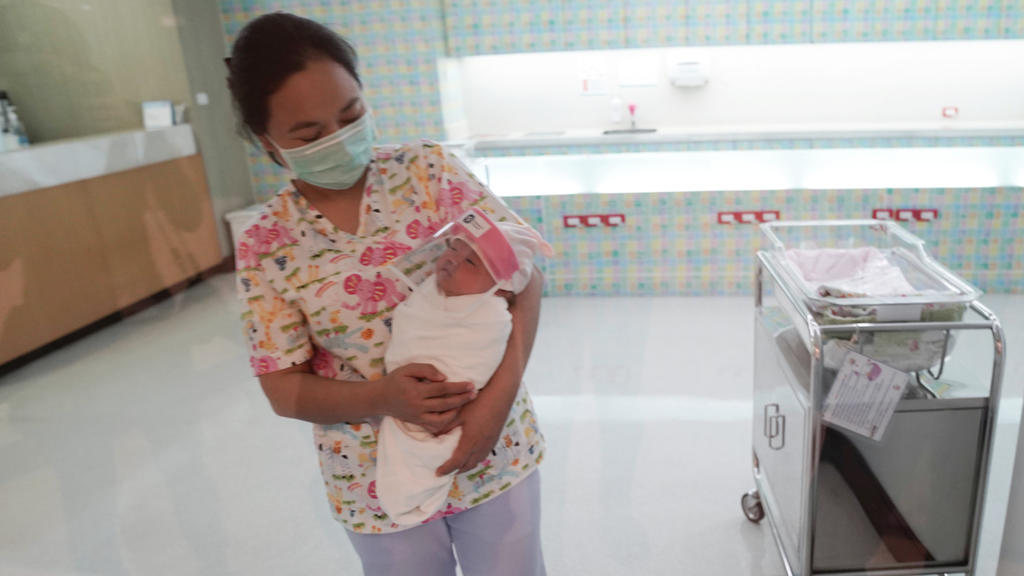 A nurse wearing a protective face mask holds a newborn baby wearing a protective face shield during the coronavirus disease (COVID-19) outbreak at the Praram 9 hospital in Bangkok, Thailand, April 9, 2020. REUTERS/Athit Perawongmetha Â