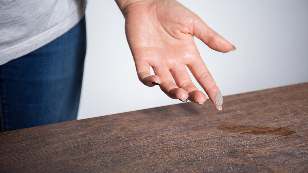 Frau streicht mit Finger über staubigen Tisch