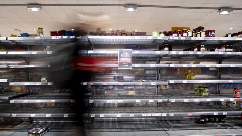 Eine Person geht in einem Supermarkt an einem fast leeren Regal vorbei. 