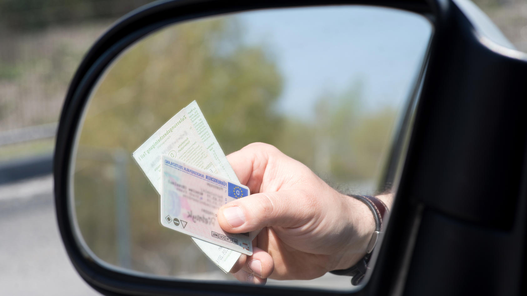 Autofahrer reicht bei Kontrolle Führerschein und Fahrzeugpapiere aus dem Autofenster.