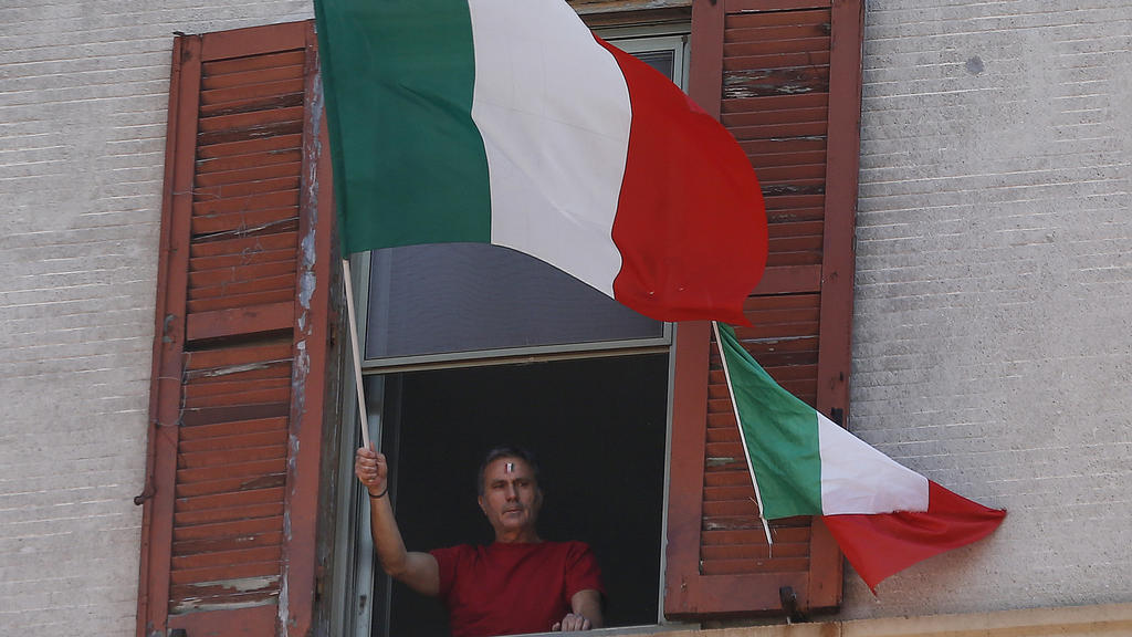 25.04.2020, Italien, Rom: Ein Mann schwenkt am Tag der Befreiung Italiens von seiner Wohnungen aus die italienische Fahne. Die üblichen Märsche in Gedenken an die Befreiung von den Deutschen Besatzern im Zweiten Weltkrieg, können während der Corona-P