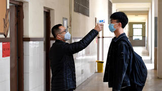 07.04.2020, China, Zhengzhou: Ein Lehrer misst die Temperatur bei einem Schüler in der Schule Nr. 9 in Zhengzhou. Die Schüler der Abschlussjahrgänge können nach der Ausgangssperre die Schule wieder besuchen. Erstmals seit dem Ausbruch der Corona-Pandemie hat China keine neuen Todesopfer mehr gemeldet. Foto: Li An/XinHua/dpa +++ dpa-Bildfunk +++