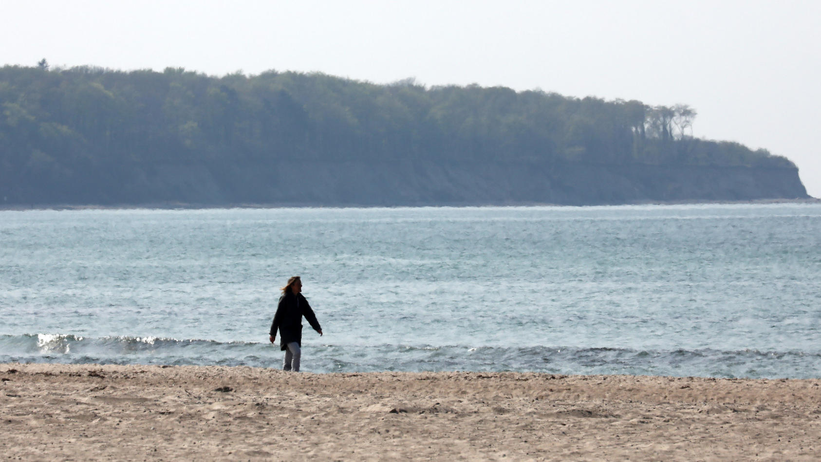 27.04.2020, Mecklenburg-Vorpommern, Warnemünde: Ein Frau geht am menschenleeren Strand spazieren, wo vor einigen Tagen noch Strandkörbe gestanden sind. Unklare Vorgaben sorgen bei den Strandkorbvermietern für Verwirrung: Während der eine seine Möbel 