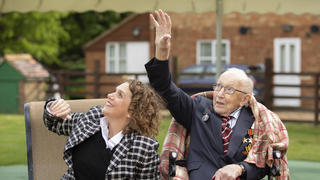 In this photo issued by Capture the Light Photography, showing Second World War veteran Captain Tom Moore with his daughter Hannah, as they react to Battle of Britain Memorial Flight flypast of a Spitfire and a Hurricane passing over his home as he celebrates his 100th birthday, in Marston Moretaine, Britain, Thursday April 30, 2020.  Captain Tom became a national hero having raised more than 29 million pounds (36 million dollars) for the National Health Service by walking laps around his garden ahead of his 100th birthday, during the national lockdown in response to the highly contagious COVID-19 coronavirus pandemic. (Emma Sohl/Capture the Light Photography via AP)