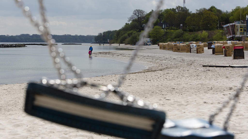 01.05.2020, Schleswig-Holstein, Kiel: Zwei Personen sind bei Sonnenschein durch eine zusammengeknotete Schaukel während ihres Spaziergangs am Strand von Kiel-Schilksee zu sehen. Sonne und Regen wechselten sich am 1. Mai 2020 in Schleswig-Holstein ab.