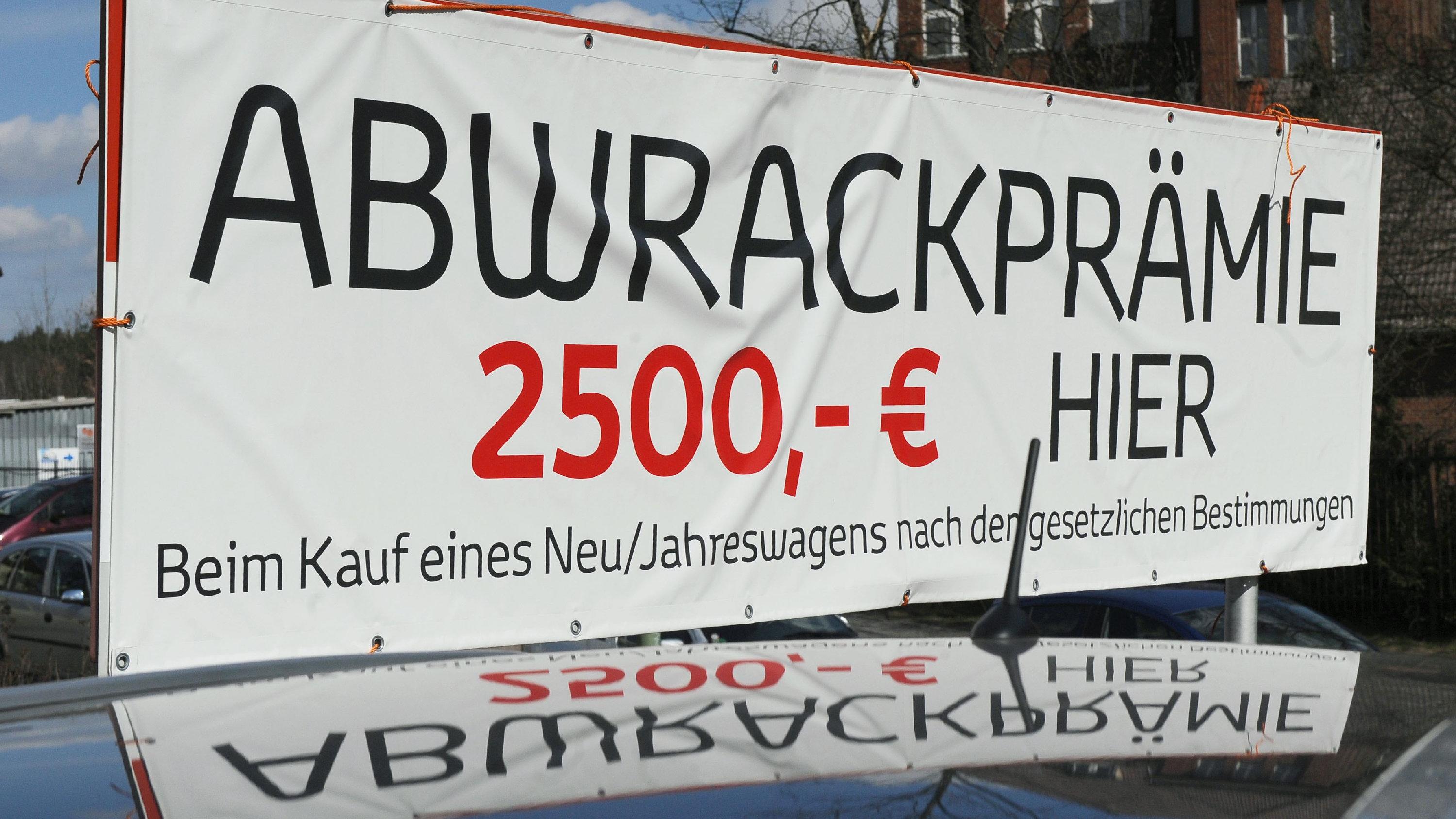 Ein Werbeschild, das auf die Gewährung der Abrackprämie hinweist, spiegelt sich am Mittwoch (25.03.2009) in Berlin auf dem Gelände eines Autohändlers im Dach eines Autos. Die staatliche Abwrackprämie zur Ankurbelung des Neuwagengeschäfts soll aufgest