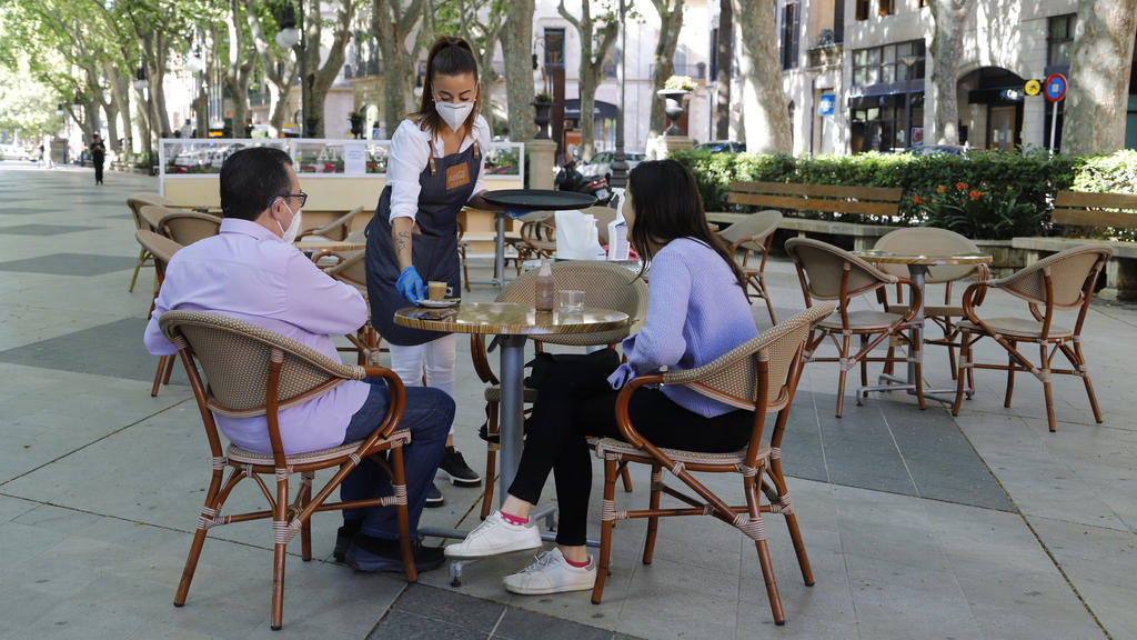 11.05.2020, Spanien, Palma: Am Tag der Wiedereröffnung serviert eine Kellnerin zwei Gästen auf der Terrasse einer Bar in Palma einen Kaffee. Ab Montag dürfen in der «Phase 1» der Lockerungen der Corona-Maßnahmen unter anderem Bars, Restaurants, Gesch