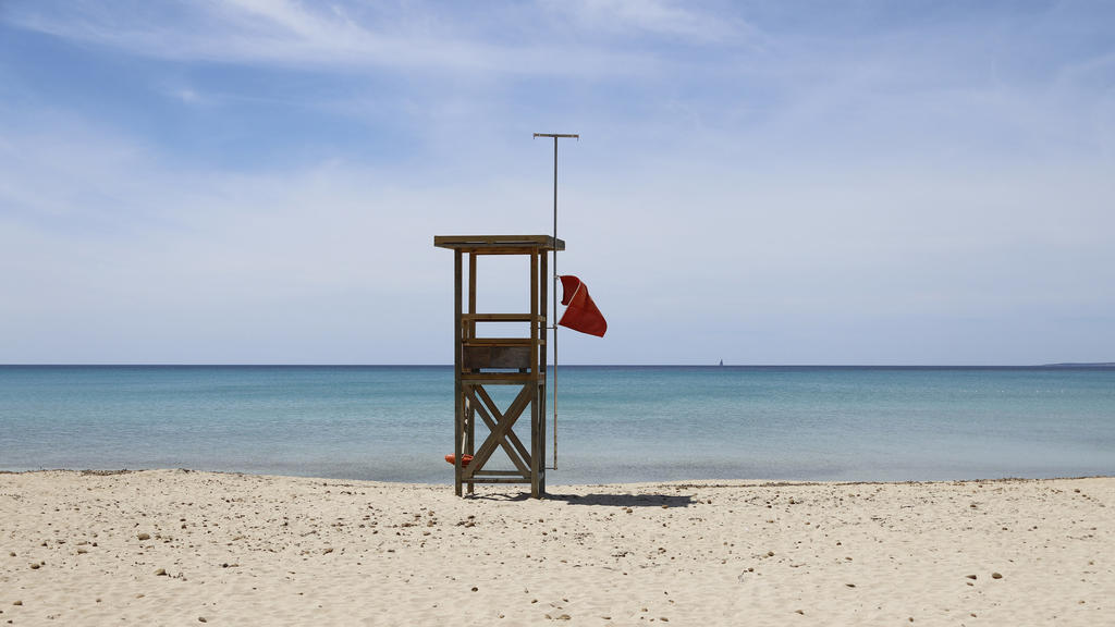 07.05.2020, Spanien, Palma: Eine rote Flagge weht am Strand von Arenal, um das Schwimmen zu verbieten. Die Abwesenheit von Touristen ist an den Stränden Mallorcas spürbar. «Das Wasser ist derzeit spektakulär transparent», sagt der Biologe Txema Broto