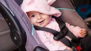 Kleines Mädchen sitzt glücklich im Autokindersitz.