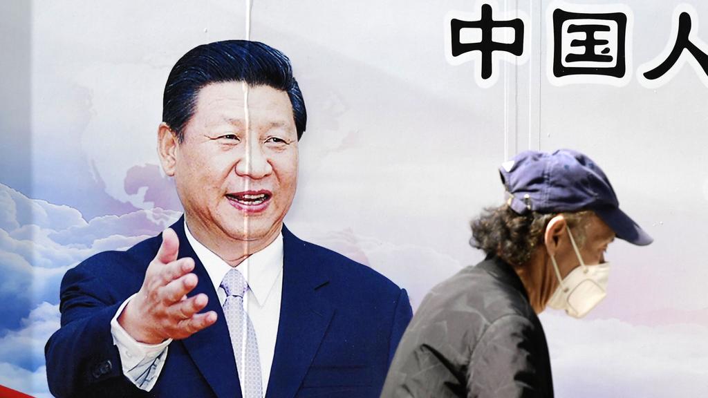 Ein Mann spaziert mit einer Maske an einem Plakat von Chinas Präsident Xinping vorbei. Foto: -/kyodo/dpa +++ dpa-Bildfunk +++