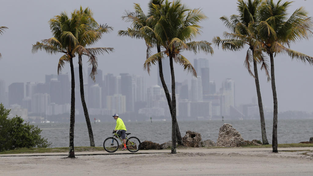 15.05.2020, USA, Miami: Ein Fahrradfahrer fährt an der Biscayne Bay entlang, während im Hintergrund die Skyline der Stadt von dunklen Wolken umhüllt ist. Ein Tiefdruckgebiet bewegt sich in Richtung der Bahamas und könnte zum ersten benannten Sturm de