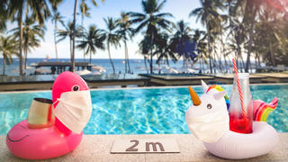Zwei Schwimmtiere sitzen mit Corona-Masken am Pool