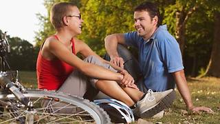 Ein Paar macht Pause beim Radfahren, sie unterhalten sich in einer Wiese.