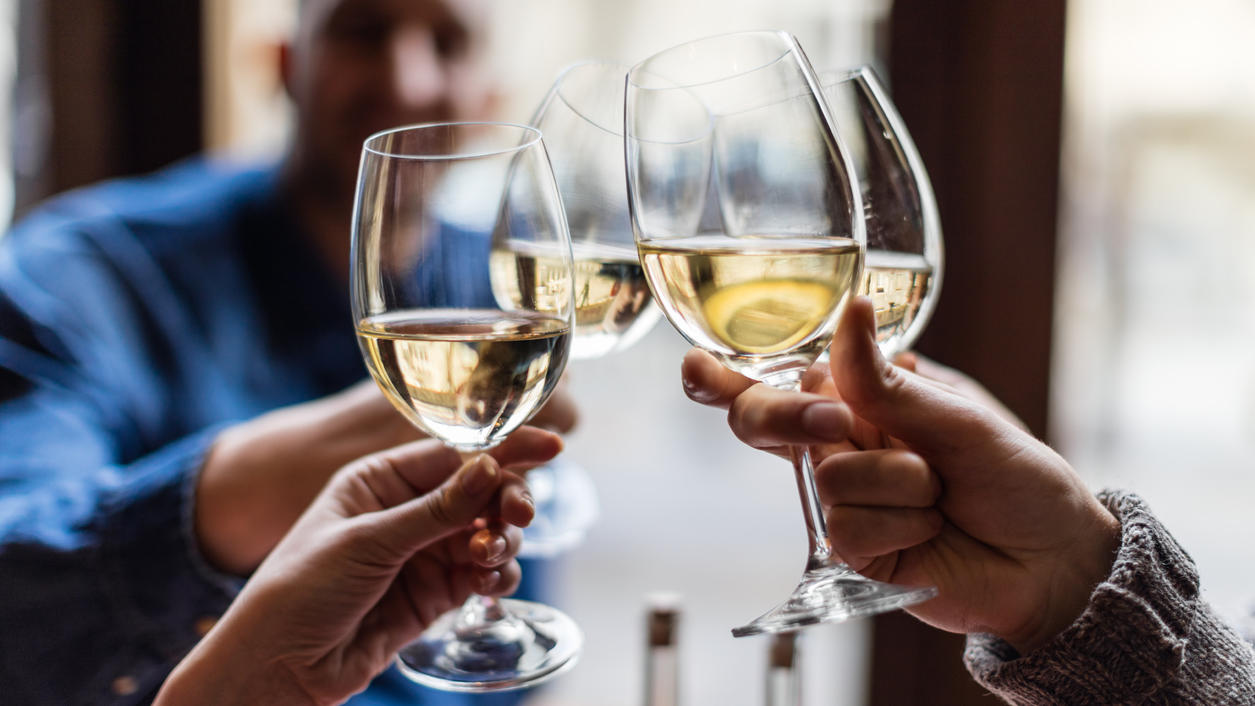 Friends toasting each other with white wine, smiling, sitting in restaurant
Freunde sitzen in einem Restaurant und stoßen mit Weißwein an.