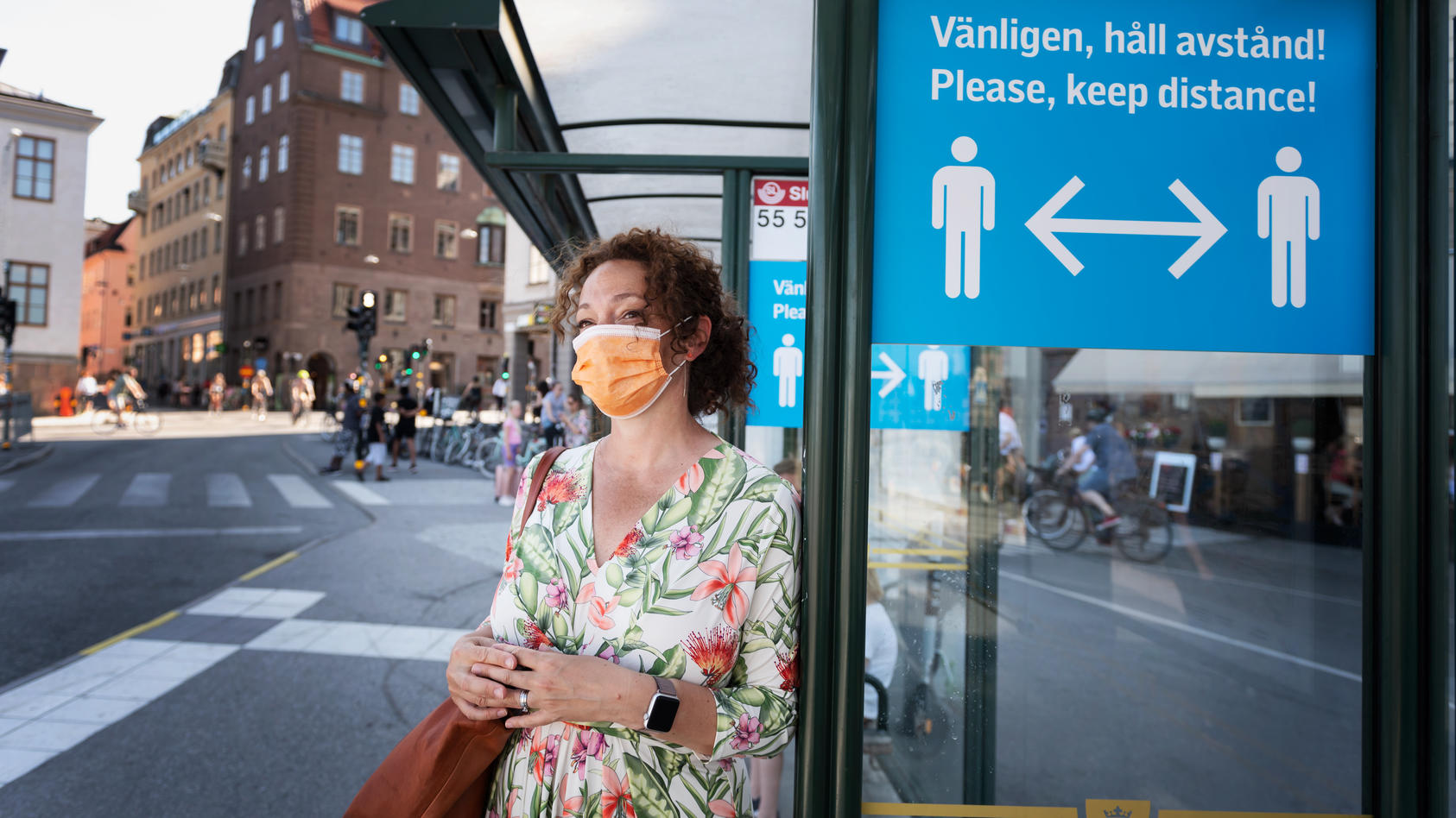 Frau steht mit Mundschutz an einer Bushaltestelle in Stockholm.