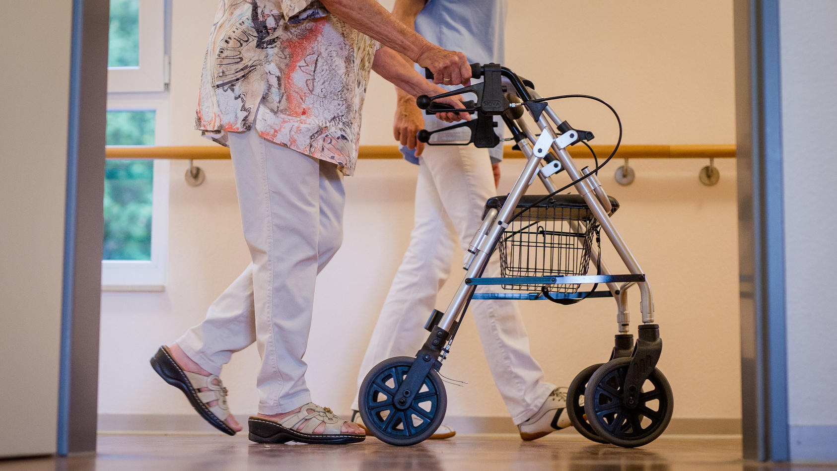 Eine Pflegekraft geht in einem Pflegeheim mit einer älteren Dame über einen Korridor. Foto: Christoph Schmidt/dpa