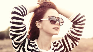 Portrait of a young redhead girl in sunglasses and striped sweater at outdoor in autumn time