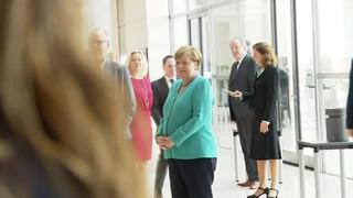 Angela Merkel schmunzelt, während Aktivisten für den Kohleausstieg protestieren.