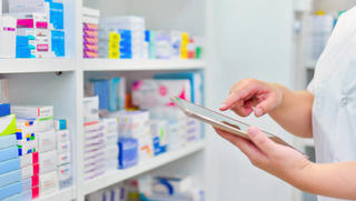 Apothekerin sucht mit einem Tablet die Medikamente aus dem Regal