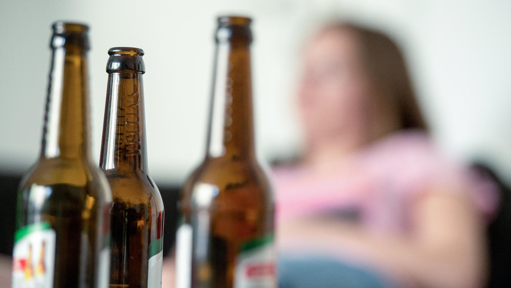 SYMBOLBILD - 28.05.2016, Berlin: Eine junge Frau sitzt hinter leeren Bierflaschen. Die Corona-Pandemie erhöht Experten zufolge das Risiko für Alkohol- und Drogenmissbrauch sowie das Zocken im Online-Casino. (zu dpa: «Suchthilfe zum Internationalen Ta