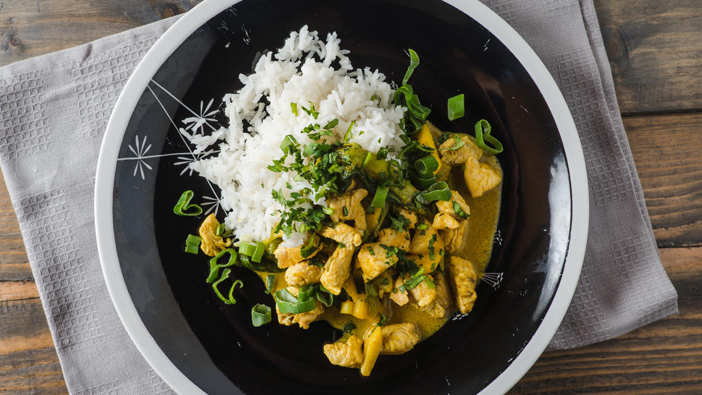 Delicious turkey mango curry with rice on a black plate