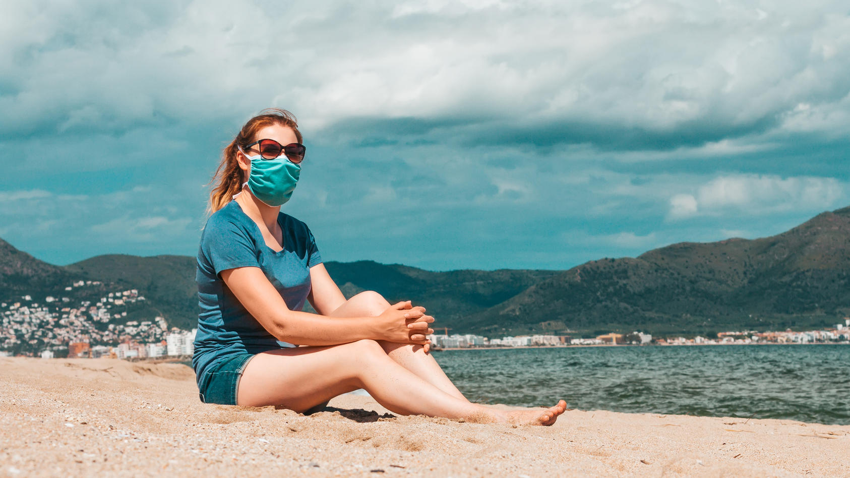 Frau mit Maske sitzt am Strand