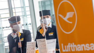 ARCHIV - 03.06.2020, Bayern, München: Zwei Lufthansa-Mitarbeiterinnen mit Mund-Nasen-Sschutzmaske und hinter Plexiglasscheiben fertigen am Flughafen-Terminal 2 die Gäste für den Flug in die USA ab.  Das Dax-Gründungsmitglied Lufthansa muss Platz machen für die Deutsche Wohnen. Der Abstieg aus der deutschen Börsenliga fällt für die Fluggesellschaft in eine schwierige Phase. (zu dpa «Ende einer Ära: Lufthansa steigt aus dem Dax ab») Foto: Peter Kneffel/dpa +++ dpa-Bildfunk +++
